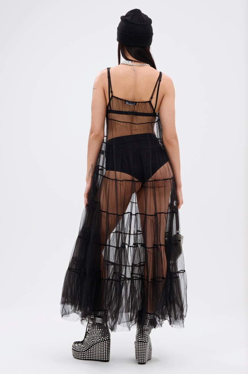 A person faces away, wearing the PERFECT FOR LAYERING TULLE MAXI DRESS over black underwear, paired with a black beanie, studded platform boots, and holding a small handbag against a plain white background.