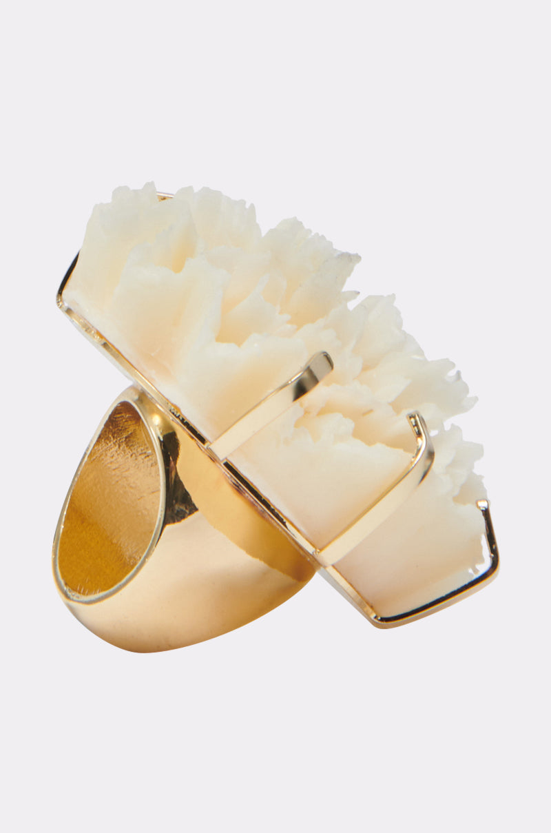 The IN BLOOM RING features a large textured white crystal-like stone set in four gold prongs atop a faux gold band, creating a striking statement accessory shown against a plain light background.