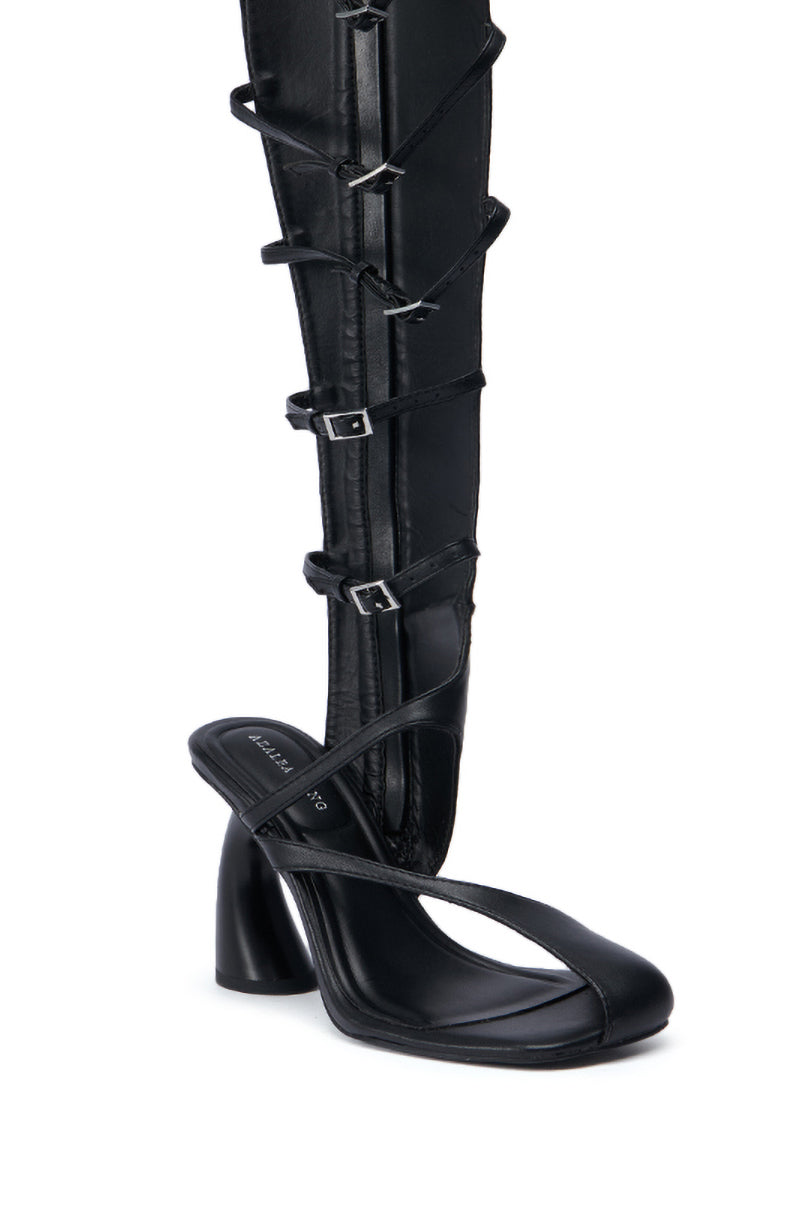 The AZALEA WANG ANDRIUS BLACK GLADIATOR SANDAL is a black heeled shoe with a distinct gladiator design, incorporating multiple straps and buckles that extend upward in a boot-like style. Crafted from faux leather, it features an open toe and chunky heel for bold elegance.
