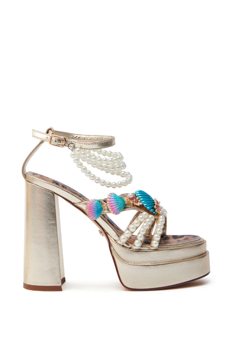 The AZALEA WANG ARLETH GOLD SANDAL features metallic gold straps, pearl embellishments, colorful shell decorations, a chunky heel, and a stacked platform sole. An ankle strap with additional pearl strands enhances the decorative flair.