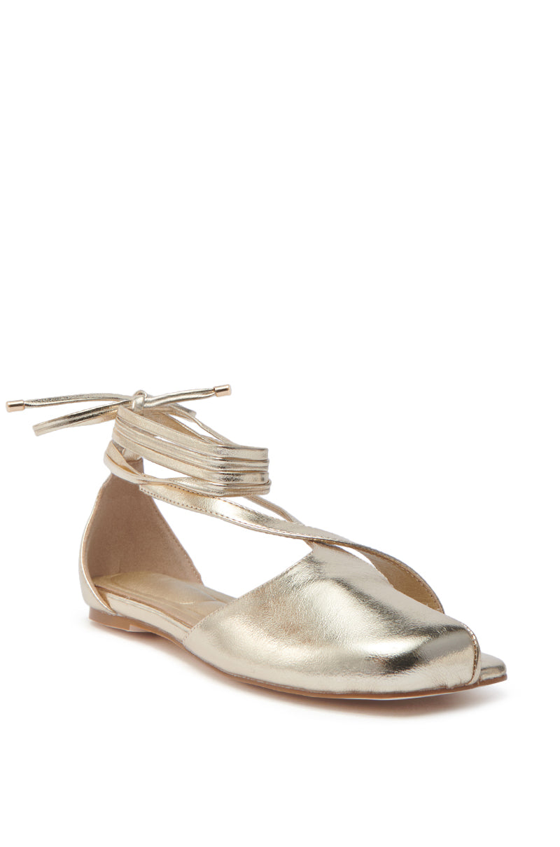 The AKIRA Aulora Gold Flat Sandal with Peep Toe showcases a peep toe design, wraparound ankle straps with sleek metal tips, a shiny metallic finish, and a low-profile faux leather sole, exuding modern elegance.