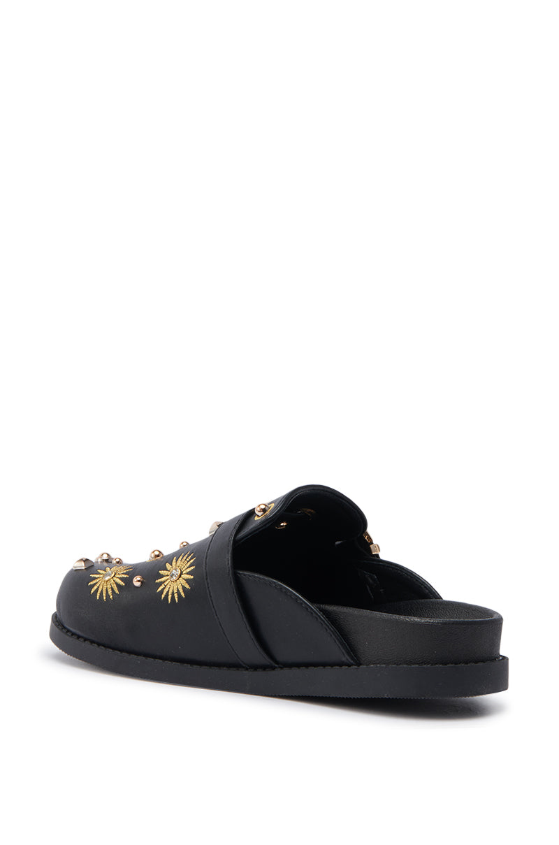 The AZALEA WANG TROUVER BLACK GOLD STARBURST FLAT is a black faux leather slip-on sandal with a closed toe, open back, flat sole, and gold starburst embellishments on the upper, shown angled from the rear.