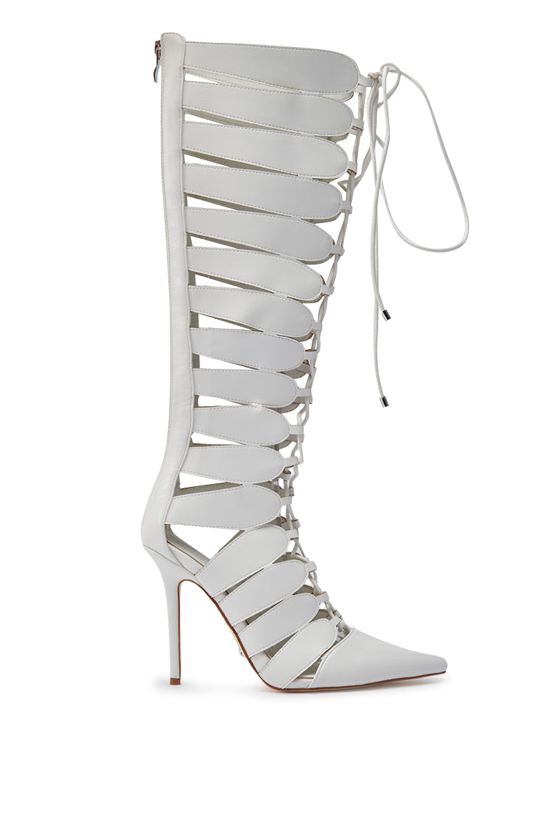 The AZALEA WANG BASTIAN WHITE BOOT is a knee-high, gladiator-style faux leather boot featuring a stiletto heel, pointed toe, front lace-up closure, multiple horizontal straps, and open sections.