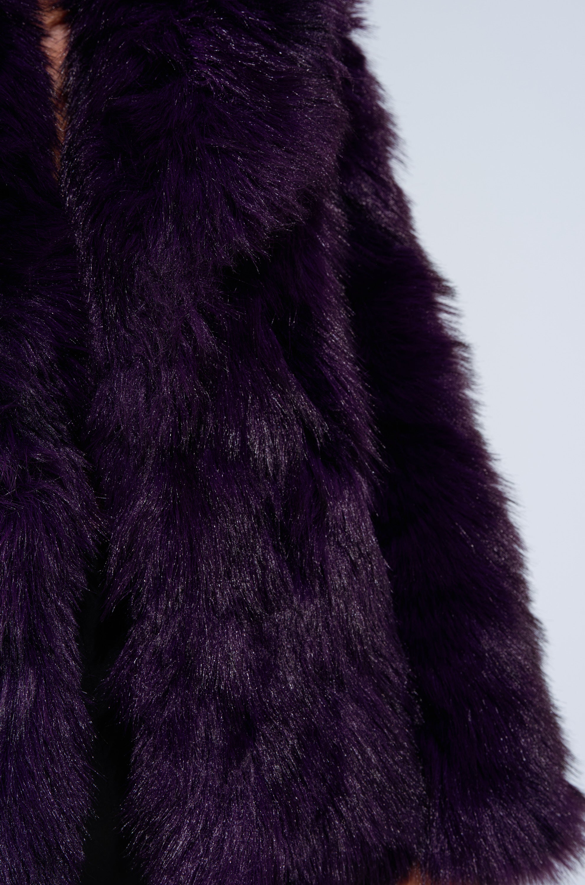 Close-up of a person wearing the SHORTIE FUR COAT, an oversized purple faux fur design. The image highlights the coat's visible plush texture and focuses on the torso against a light background.