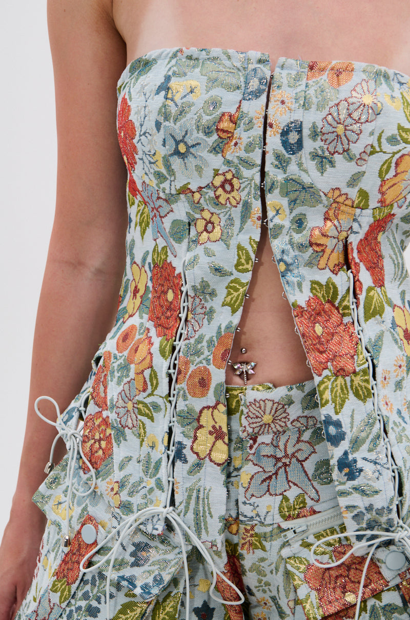 A close-up of a person wearing the MARTHA FLORAL CORSET, featuring colorful embroidered flowers, open lacing, and a visible belly button piercing.