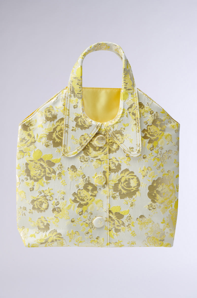 The COME WITH ME BROCADE PURSE is a vintage-inspired handbag styled like a floral-patterned shirt. It features a cheerful yellow and white color scheme, with a handle resembling a shirt collar, adding charm and elegance to any outfit.