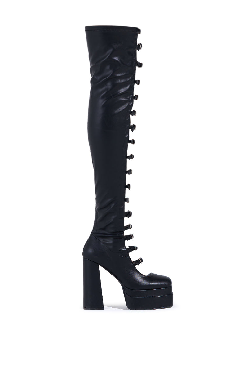 The AZALEA WANG BRYNNE BLACK CHUNKY PLATFORM BOOT is a sleek, modern thigh-high made from faux leather with a glossy finish. It features rhinestone buckles up the front and a chunky high heel.
