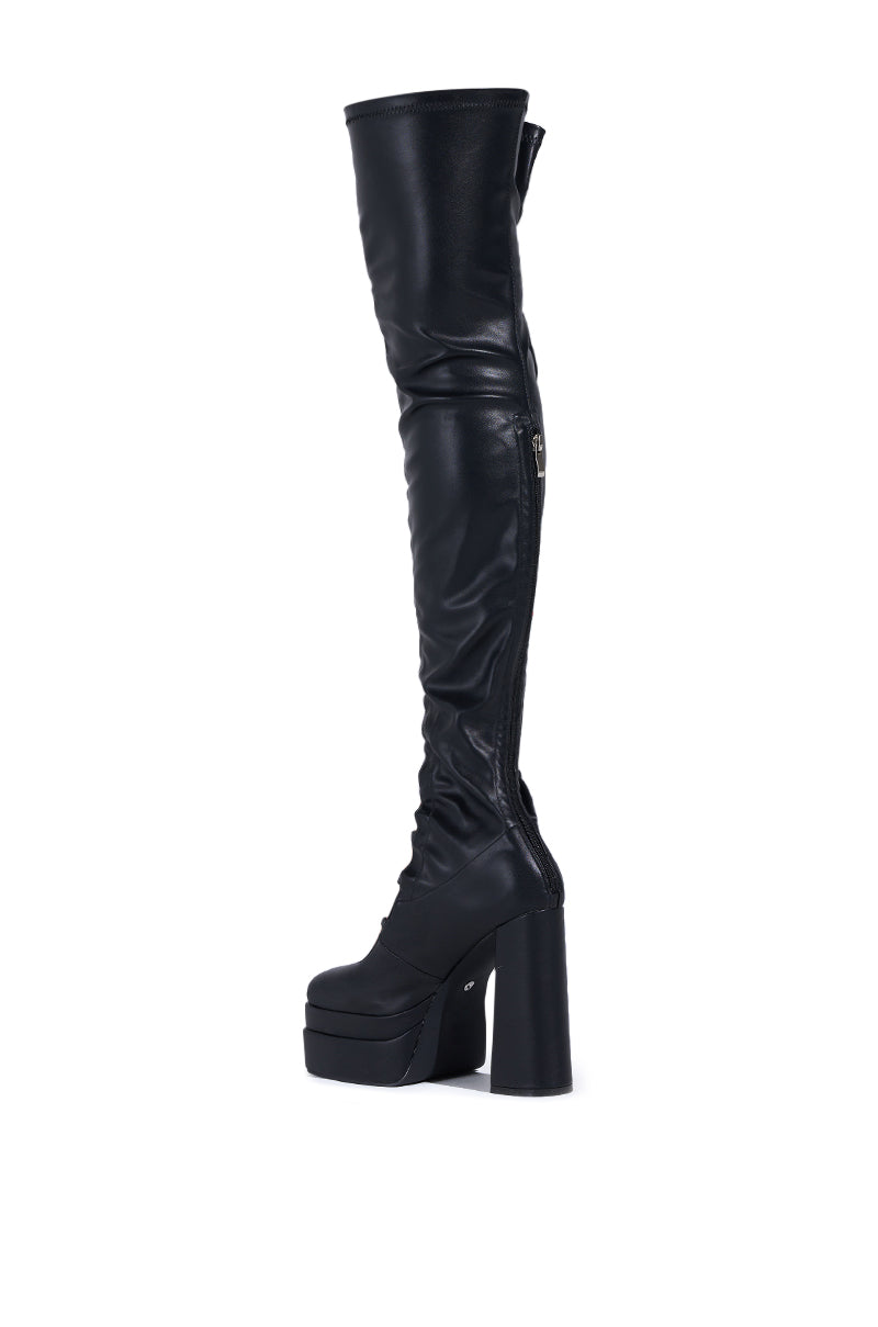 The AZALEA WANG BRYNNE boot is a black, thigh-high chunky platform in faux leather, featuring rhinestone buckles, a high heel, and an inner side zipper. It boasts a smooth, shiny finish that extends above the knee and is displayed on a plain white background.