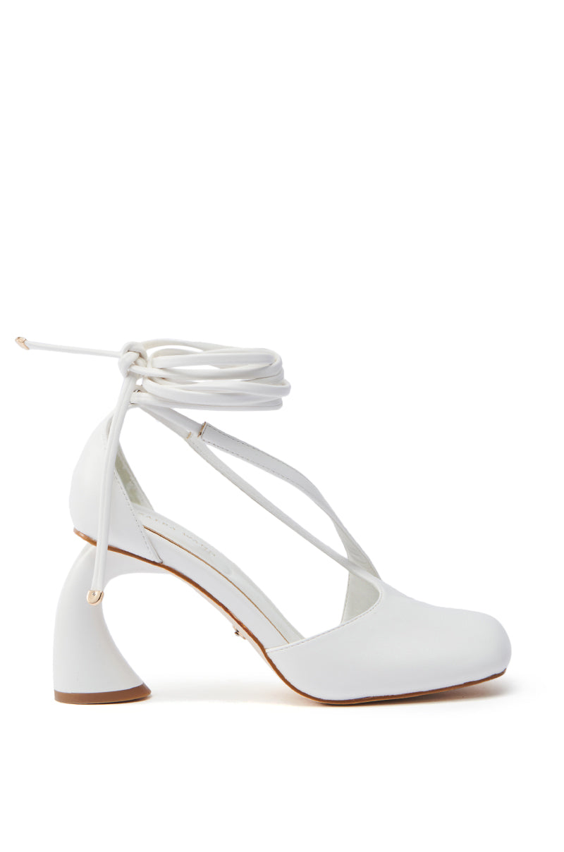 The AZALEA WANG BUIKY WHITE OPEN TOE PUMP is a single white high-heeled shoe featuring a unique sculpted heel, crisscross straps on the front, and long laces that wrap around the ankle. Crafted from faux leather, it is showcased on a plain white background.
