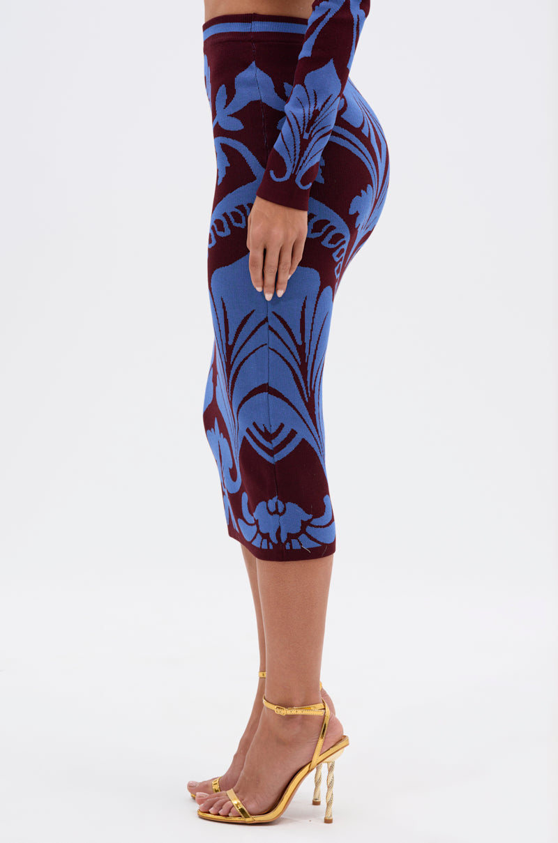 A person wears the GIVE ME LOVE MIDI SKIRT—a fitted, knee-length pencil skirt in cobalt blue damask—paired with gold high-heeled sandals and stands against a plain white background.