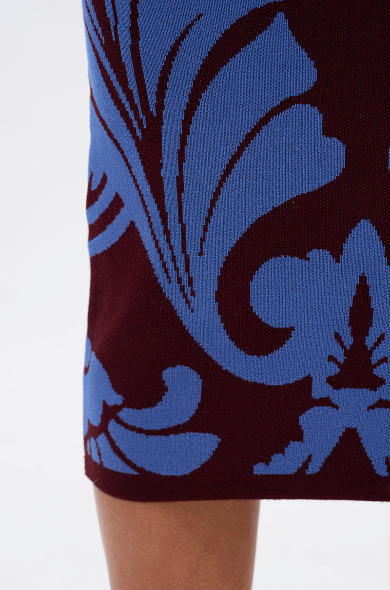 Close-up of the GIVE ME LOVE MIDI SKIRT, showcasing a bold cobalt blue damask pattern on dark burgundy fabric, high-rise elastic waistband, and part of a bare leg at the bottom edge.