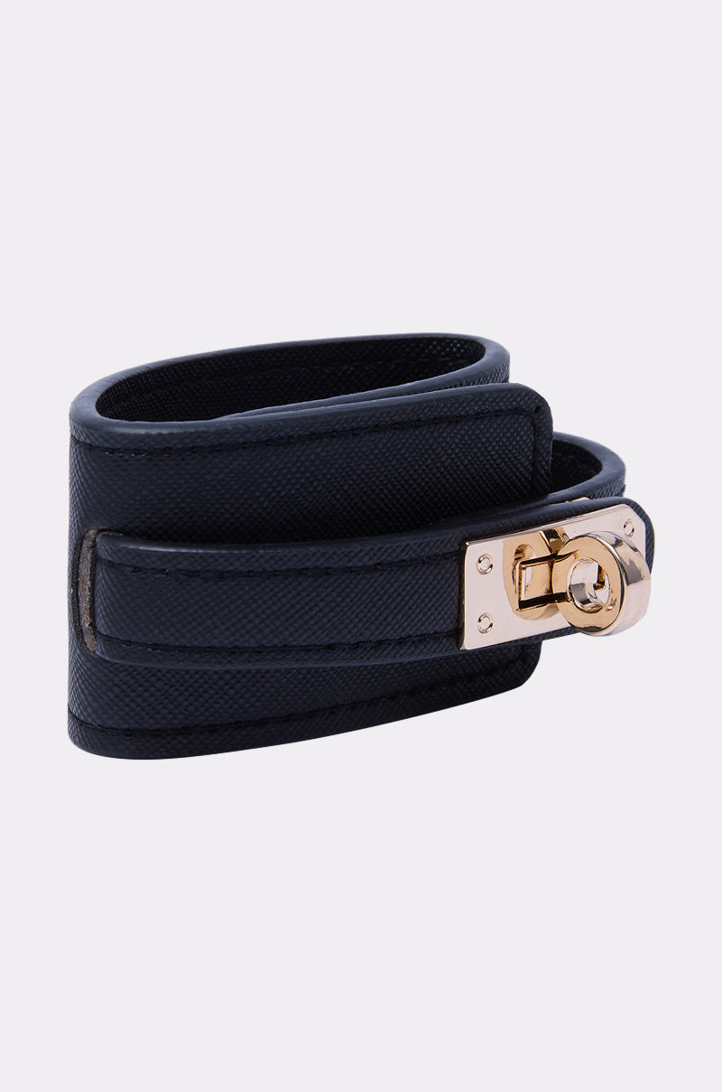 The DESIGNER BRACELET features dark navy textured leather and a gold-toned metal clasp, showcased on a light gray background.