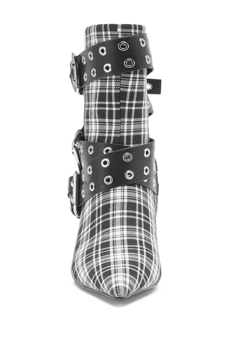 The AZALEA WANG CHALKIS BLACK WHITE PLAID BUCKLE WEDGE BOOTIE features a black and white plaid design, pointed toe, wide black straps with silver grommets, and large metal buckles for a bold, modern look.