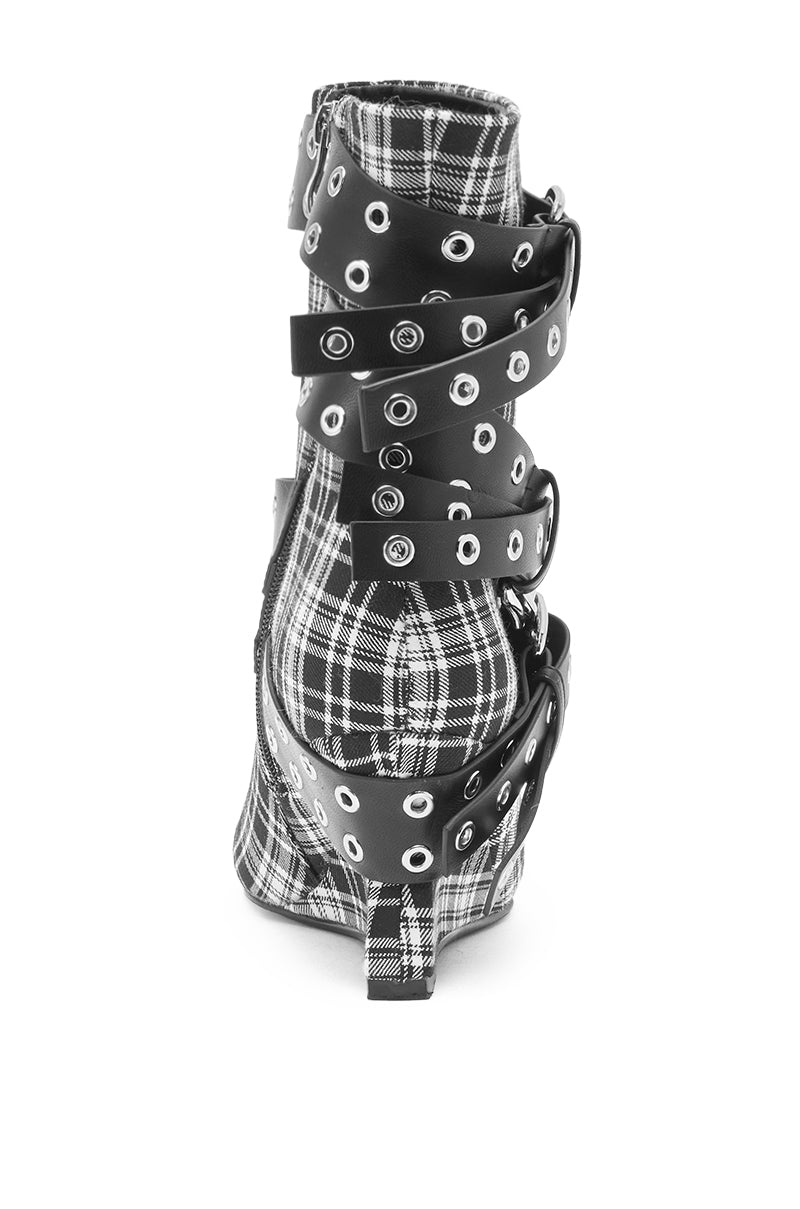 The AZALEA WANG CHALKIS BLACK WHITE PLAID BUCKLE WEDGE BOOTIE features a black and white plaid pattern, high wedge heel, multiple black buckle straps with silver grommets, and is shown from the back on a white background.