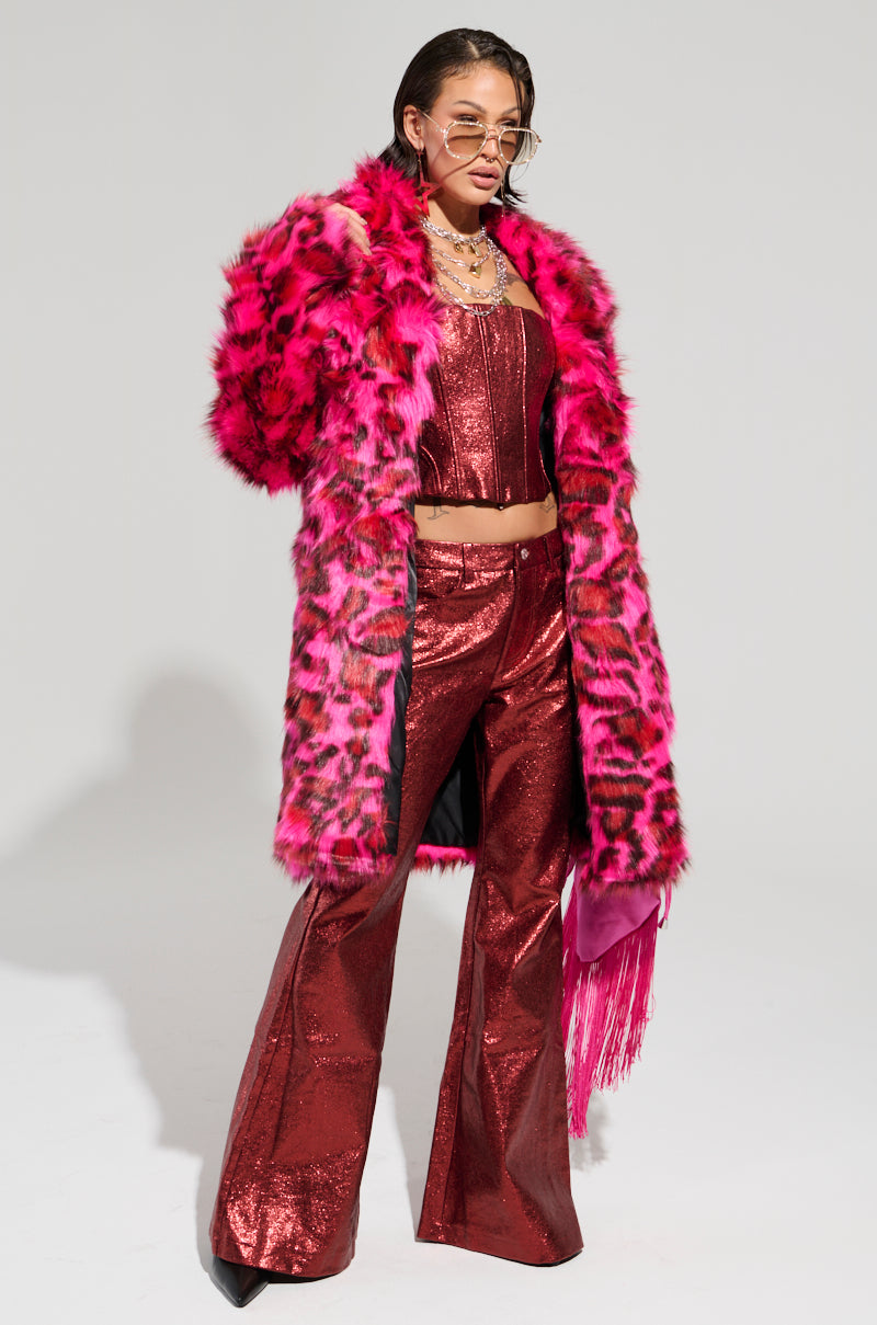 A person wearing the CHEETAH DYNASTY PINK MULTI FAUX FUR JACKET with a cheetah print pattern over a shiny red sequin two-piece outfit. They accessorize with layered necklaces and large sunglasses, striking a confident pose against a plain background.