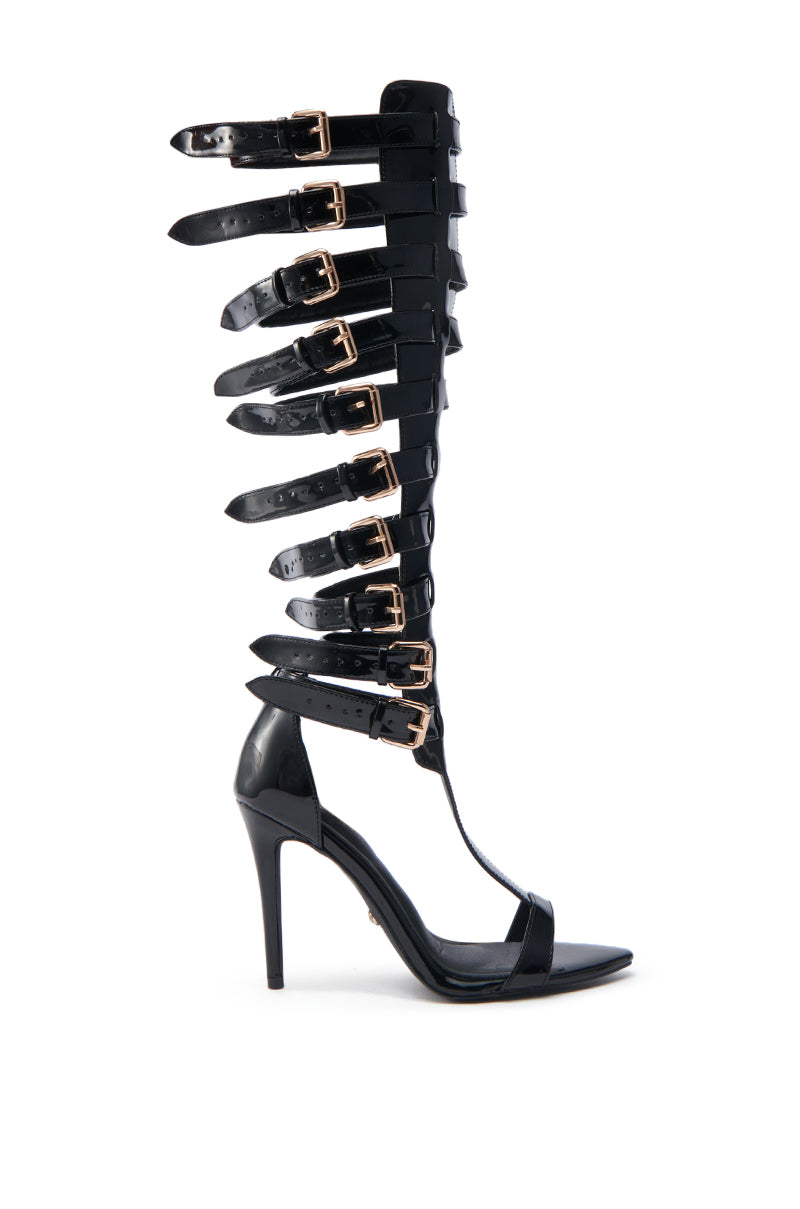 The AZALEA WANG CHRELLI BLACK OVER THE KNEE SANDAL features a tall gladiator-style shaft with multiple buckle straps, sleek faux patent leather, an open toe, high heel, and a glossy black finish.