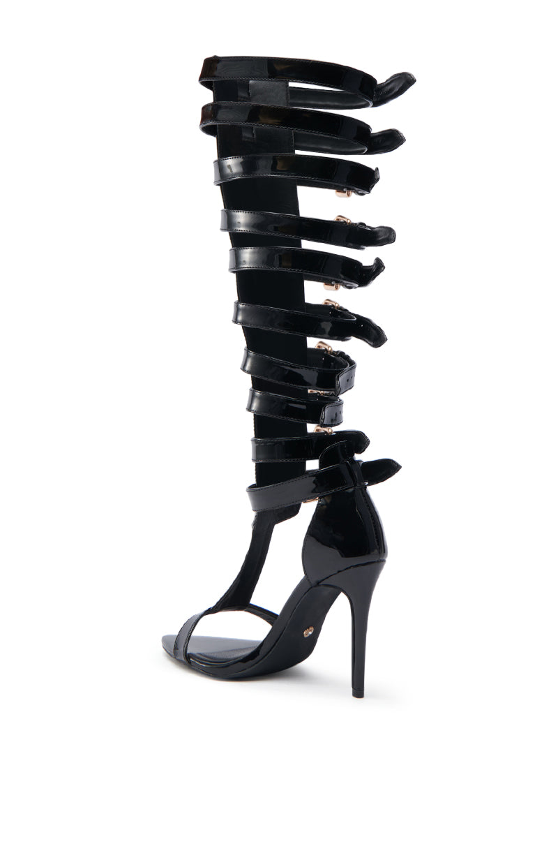 The AZALEA WANG CHRELLI BLACK OVER THE KNEE SANDAL is a faux patent leather gladiator sandal with shiny adjustable buckle straps up to the knee, shown on a white background.