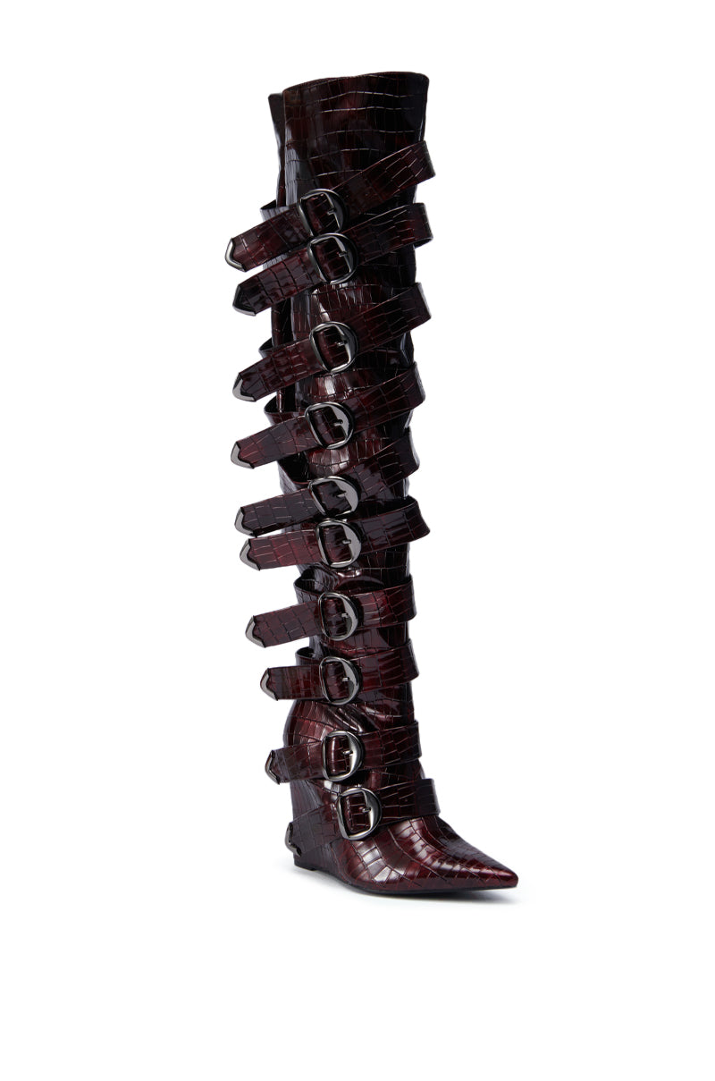 The AZALEA WANG CINZIA RED WEDGE BOOT features tall, dark red faux crocodile leather, a pointed toe, multiple horizontal straps, and silver buckles running up the thigh-high shaft.