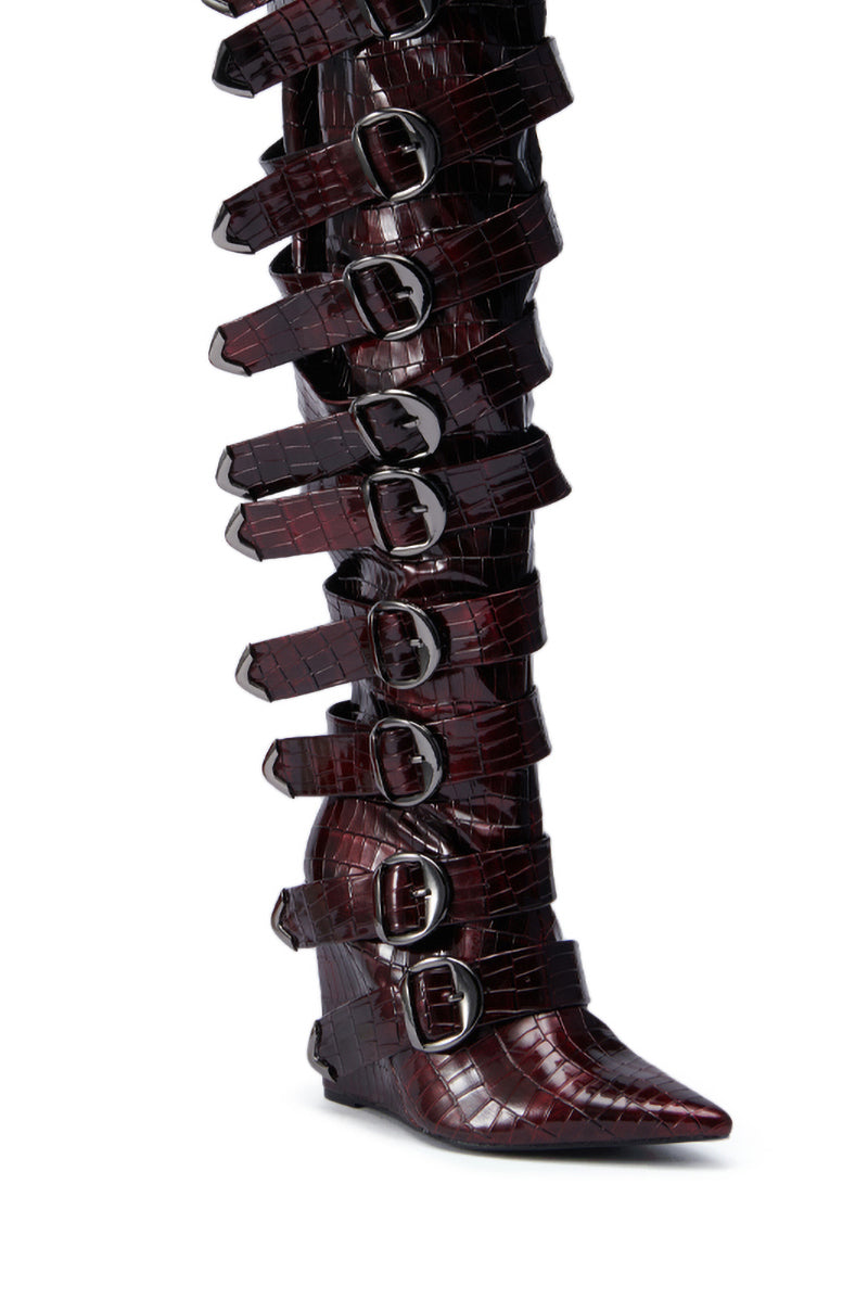 The AZALEA WANG CINZIA RED WEDGE BOOT WITH BUCKLE DETAIL is a tall, pointed-toe thigh-high boot in red faux croc leather, featuring nine wide straps with large silver buckles up the length and a wedge heel.