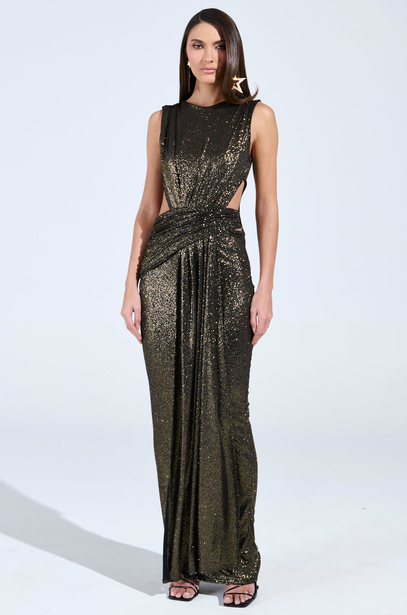 A woman wears the Cross My Heart Maxi Dress with cutouts, a sleeveless metallic black gown featuring side cutouts and a draped waist. She has long straight hair and complements her look with star-shaped statement earrings against a plain light background.