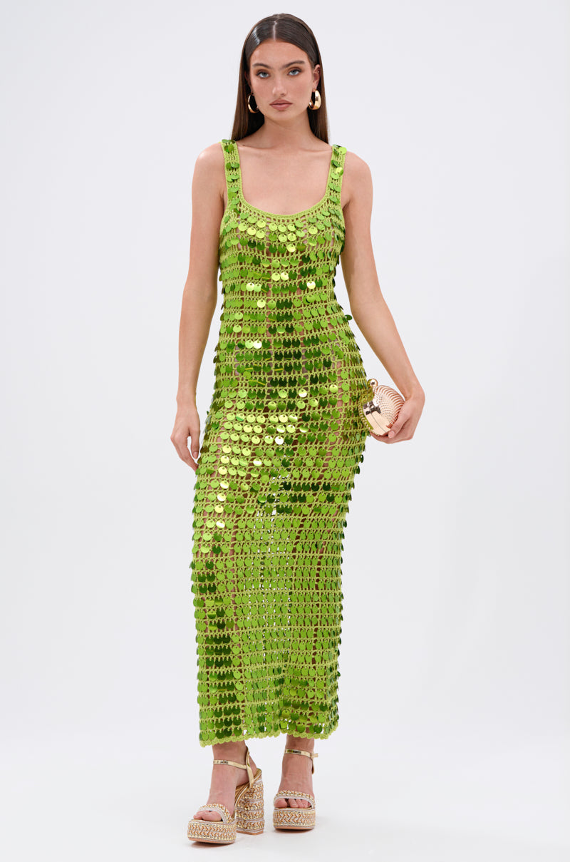 A woman stands against a white background in the SHINE BRIGHT CROCHET SEQUIN MAXI DRESS IN GREEN with platform sandals and a gold clutch—ready to light up any event.