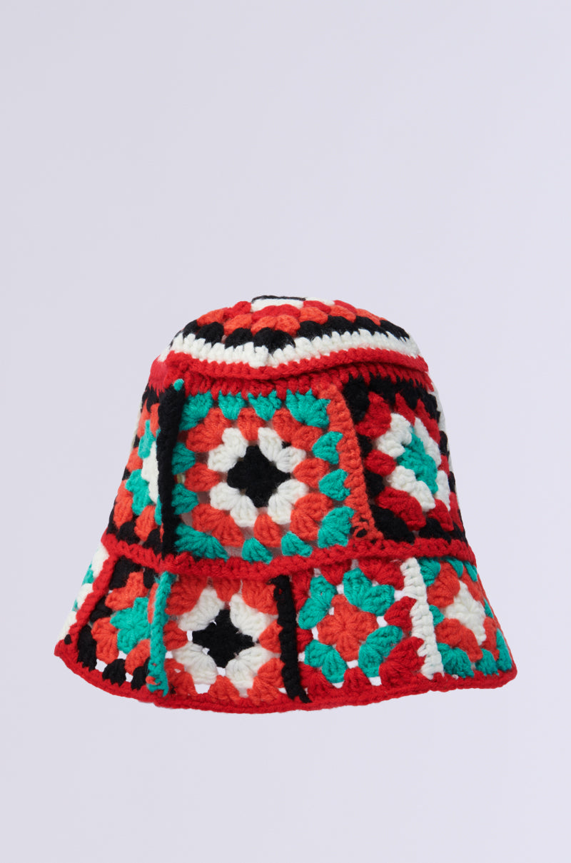 The CROCHET BUCKET HAT features a vibrant patchwork pattern with geometric designs in red, black, white, and mint green squares on a mosaic style. Its neutral light gray background enhances the colorful flair.