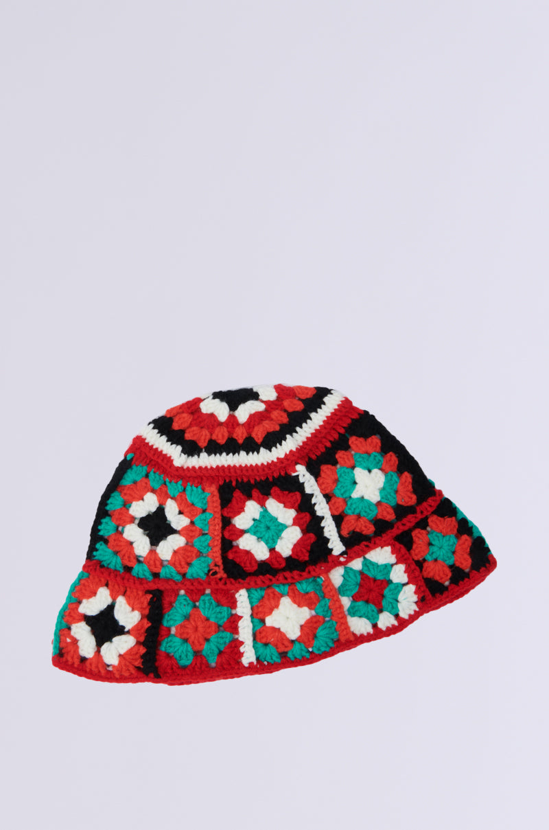 The CROCHET BUCKET HAT boasts a vibrant, floppy patchwork design with red, green, black, and white squares. The colorful geometric patterns make this accessory pop against a plain white backdrop.