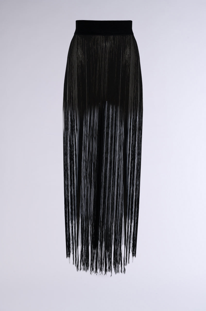 The SO FREE FRINGE BELT SKIRT features a long black design adorned with cascading fringe detailing from the elasticated wide waistband to the hem, creating a flowing and dynamic texture. The skirt's design stands out against a plain, light-colored background.