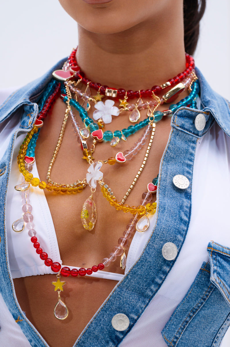A person pairs a white top and blue denim jacket with the DIDI LOVE NECKLACE, featuring multicolored beads, heart charms, flowers, and teardrop-shaped pendants.