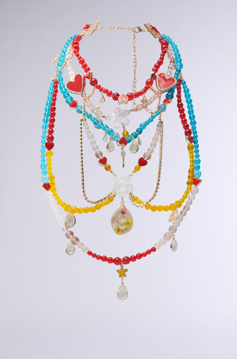 The DIDI LOVE NECKLACE showcases a colorful maximalist aesthetic with red, blue, yellow, and clear multicolored glass beads. It features heart-shaped charms, tear-shaped pendants, and gold chains for a whimsical and vibrant design.