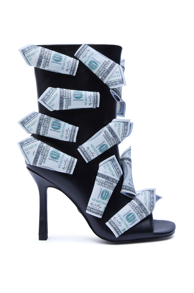The AZALEA WANG DINERO BLACK MONEY OPEN TOE BOOTIE features black high heels adorned with bands that look like folded U.S. hundred-dollar bills, offering a bold and luxurious style set against a white background.