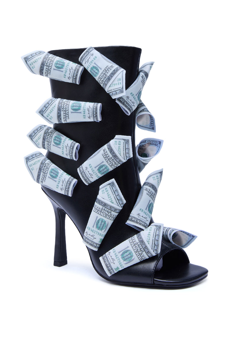 The AZALEA WANG DINERO BLACK MONEY OPEN TOE BOOTIE features faux leather and is adorned with rolled-up US hundred dollar bills around the upper, all showcased against a white background.