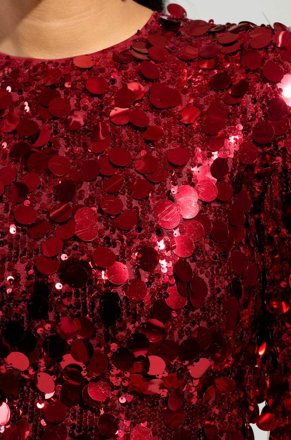 Close-up of the SHE'S ALL THAT SEQUIN MINI DRESS featuring a dazzling array of shiny red sequins that catch and reflect light beautifully. The densely arranged sequins create a lively, textured surface, making it an ideal choice for a party-ready look. At the top of the image, you can glimpse the edge of a person's neck and shoulder, suggesting its flattering bodycon fit.