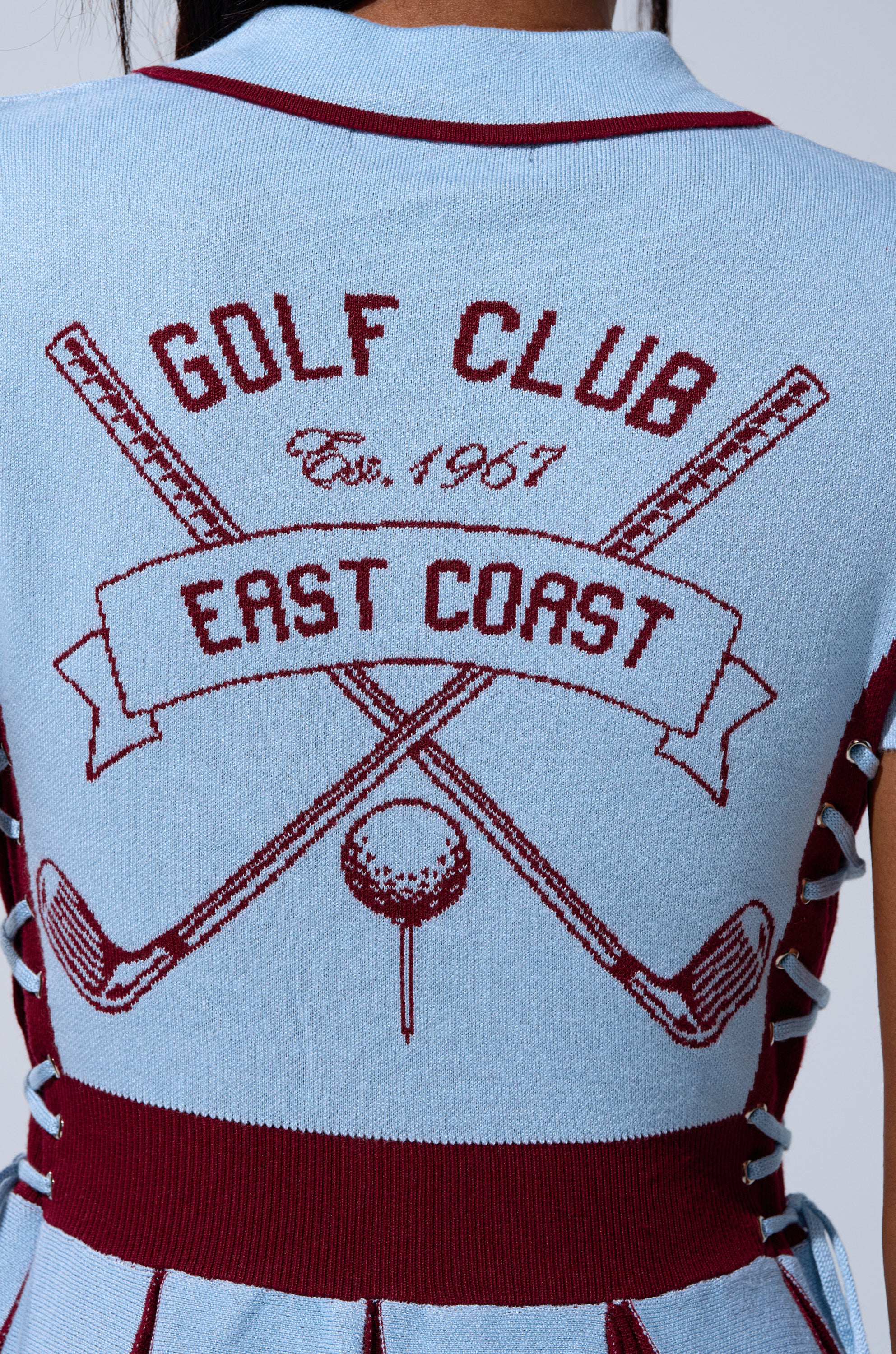 A close-up of the back of the DREKE KNIT MINI DRESS IN BLUE AND BURGUNDY, featuring maroon crossed golf clubs, a golf ball on a tee, and "GOLF CLUB" and "EAST COAST" banners—a perfect preppy look.