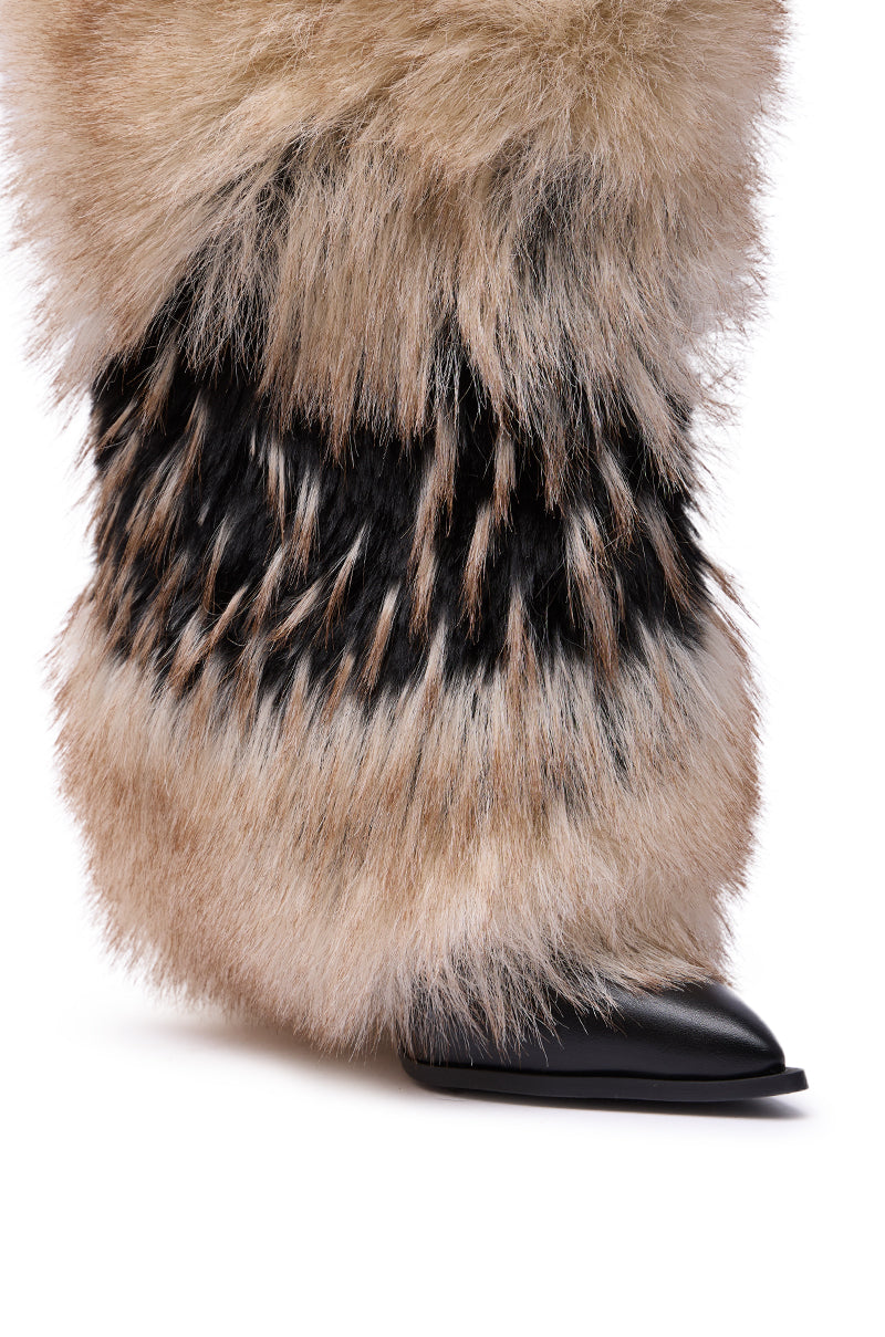 A close-up of a person wearing the AZALEA WANG EKKO MULTI FUR STILETTO BOOT—tall, plush boots featuring a mix of light brown, black, and white faux fur textures with pointed toes and a bold black tip.