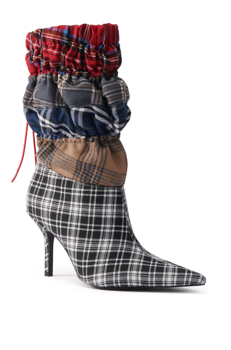 The AZALEA WANG ELADIES MULTI BOXER BOOTIE is a high-heeled, pointed-toe stiletto bootie with a black and white plaid base, featuring layered ruched heritage tartans in red, blue, and tan wrapping the ankle and calf.