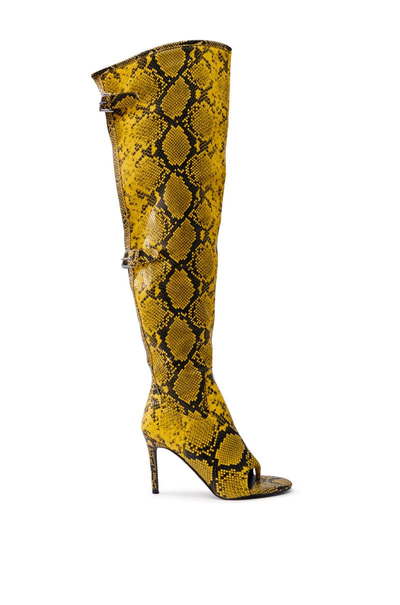 The AZALEA WANG ELIAM BOOT IN YELLOW is a striking yellow and black thigh-high boot crafted from faux snakeskin leather. It features a pointed toe, stiletto heel, chic peep-toe design, and decorative buckle accents for added flair.