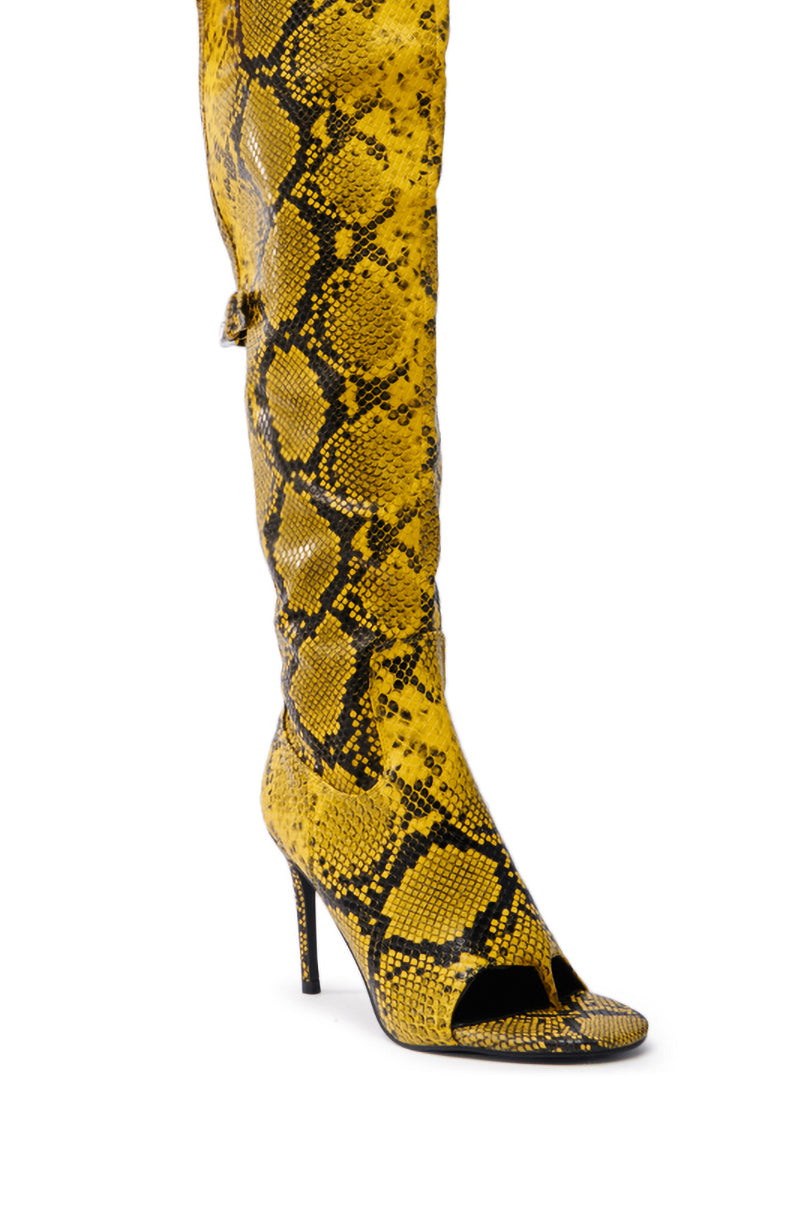 The AZALEA WANG ELIAM BOOT IN YELLOW is a chic stiletto heel with a peep-toe design, made from faux snakeskin leather in a yellow snake pattern with black accents.