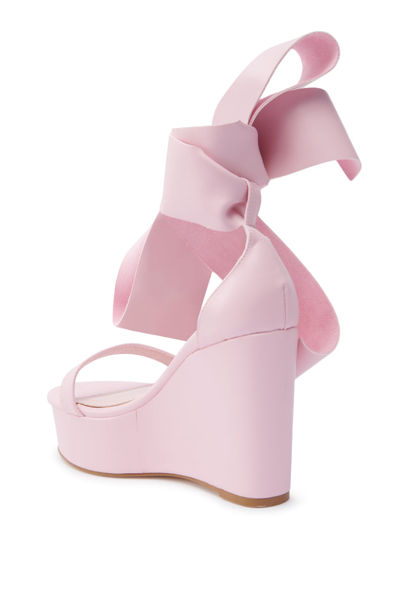 The AZALEA WANG EMEKA Pink Platform Sandal features a wedge heel and wide faux leather ankle straps tied in a large back bow, shown from a rear side angle on a white background.