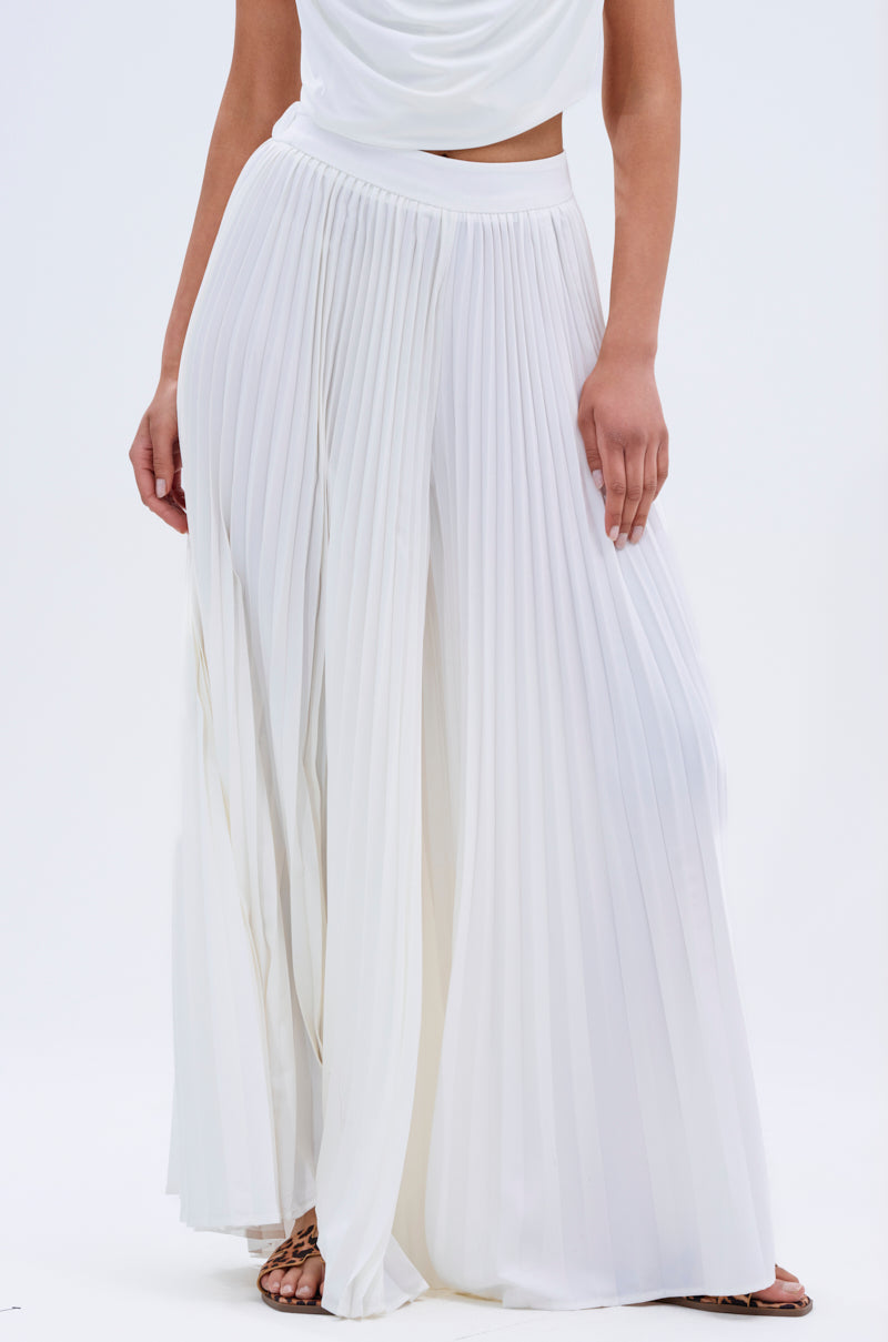 A person wearing FLY INTO THE AIR PALAZZO PANT in white with a draped white top, hand by their side. Only the lower half of their body is visible.