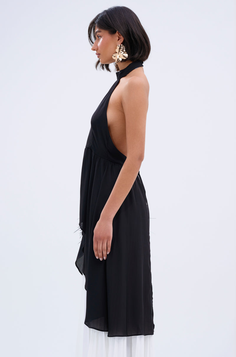A woman with a bob haircut wears the FLY INTO THE AIR BLOUSE— a sleeveless high neck black halter-style top with deep side cuts and large floral earrings, standing in profile against a plain light background.