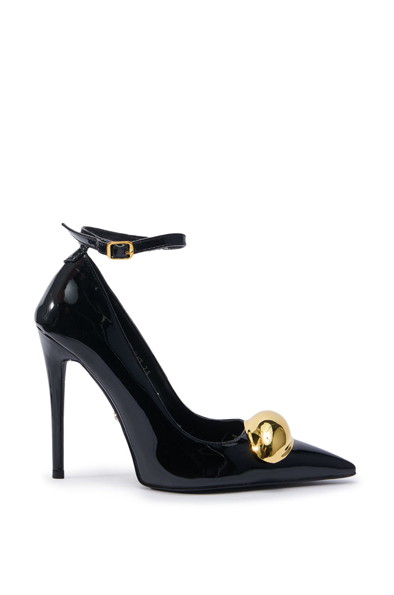 The AZALEA WANG ESMARIA BLACK STILETTO PUMP is a chic black faux leather shoe with a pointed toe and ankle strap, highlighted by a shiny gold decorative sphere near the toe. It includes a comfort cushion insole, effortlessly combining elegance and comfort. The shoe is displayed against a plain white background.