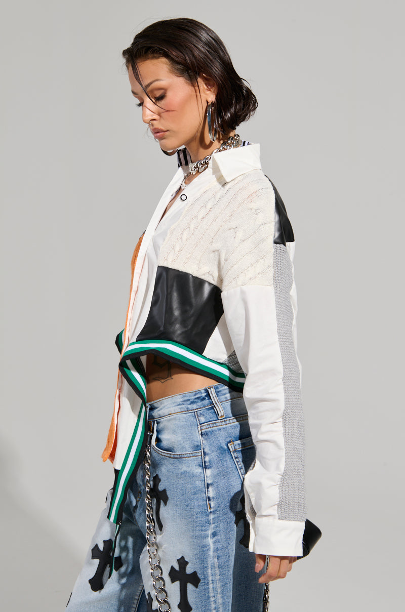 A person wearing the NEVER SEE YOU AGAIN BUTTON DOWN COLOR BLOCK SHIRT, featuring mixed textures and colors, paired with blue jeans adorned with black cross patterns. The individual has short, wet-look hair and is accessorized with hoop earrings and a choker necklace.