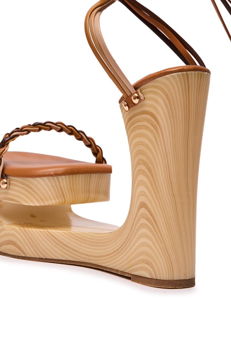 Close-up of the AZALEA WANG FANTASA BROWN HALLOW PLATFORM WEDGE STRAPPY SANDAL, featuring a high, curved brown wedge heel with a smooth, light wood grain, braided strap, and tan leather details.