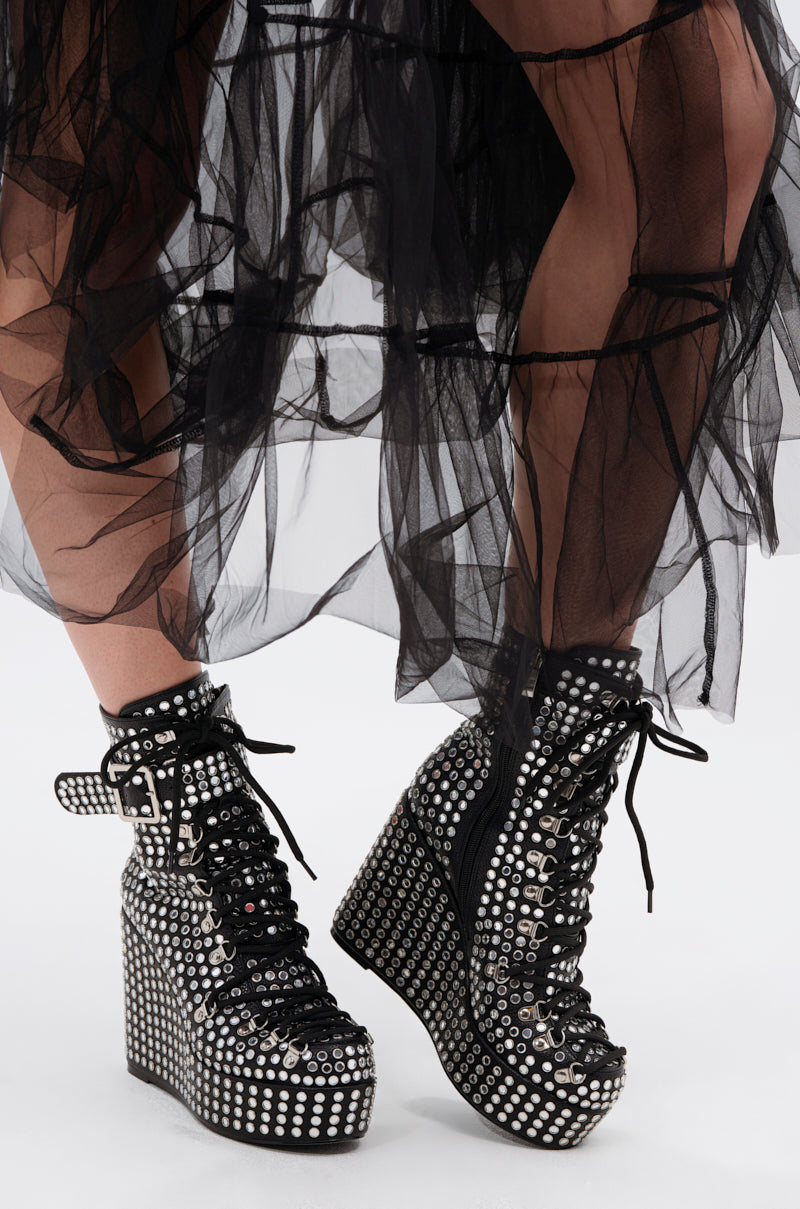 Close-up of a person wearing the AZALEA WANG FERDY BLACK PLATFORM EMBELLISHED BOOTIE with silver studs and grommets, paired with a sheer black layered tulle skirt against a plain white background.