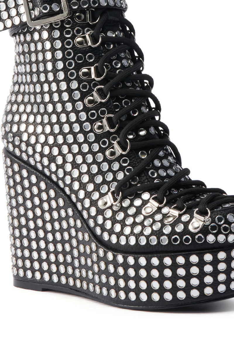 Close-up of the AZALEA WANG FERDY BLACK PLATFORM EMBELLISHED BOOTIE, a black faux leather bootie with a wedge heel, adorned with rows of metallic studs and black laces threaded through metal eyelets.