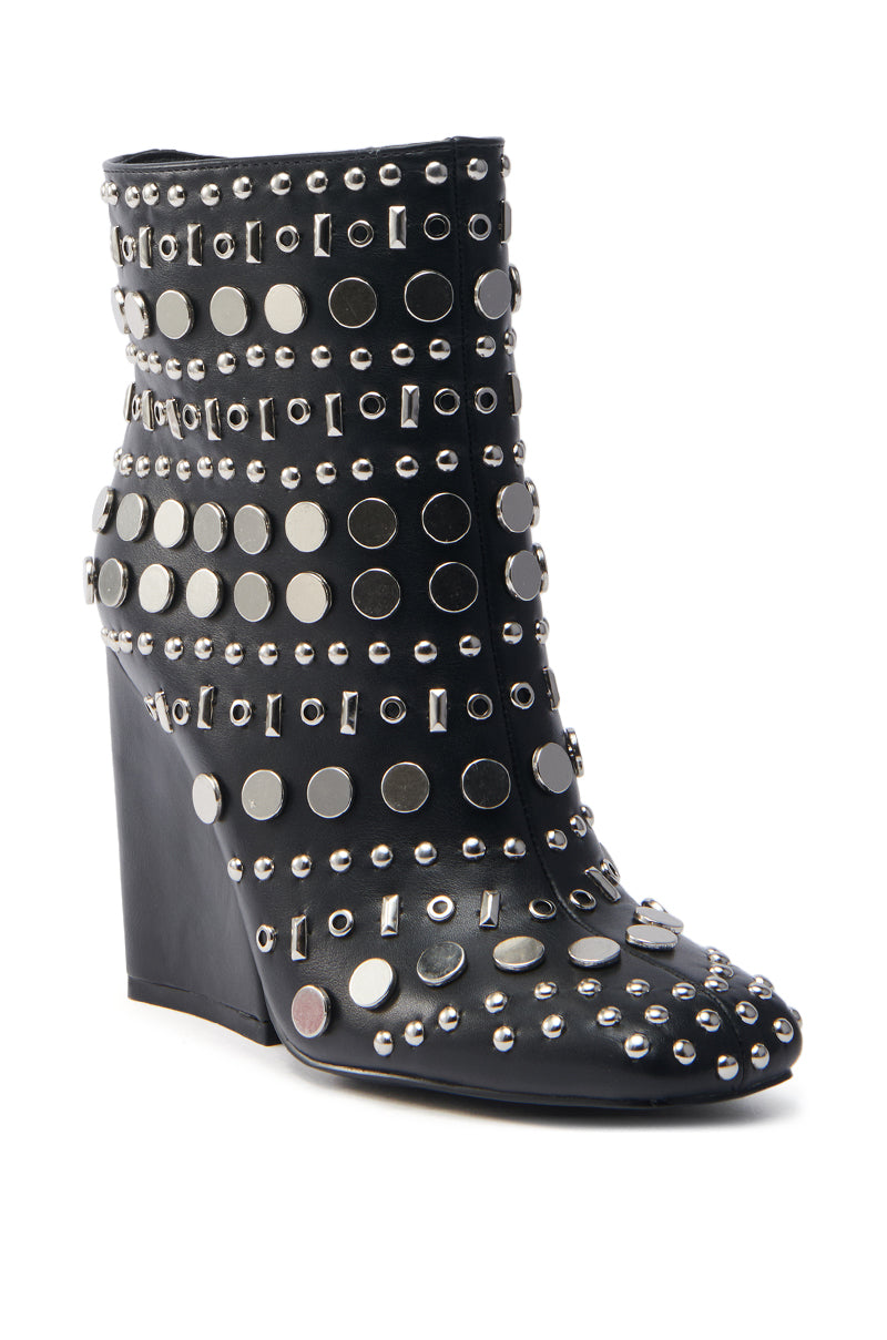 The AZALEA WANG FLETCHER BLACK SILVER METAL BOOTIE is a vegan leather ankle boot with a wedge heel, adorned with metallic silver studs and embellishments for an edgy, bold look. Its surface is richly decorated, making it a stunning piece of silver-studded footwear.