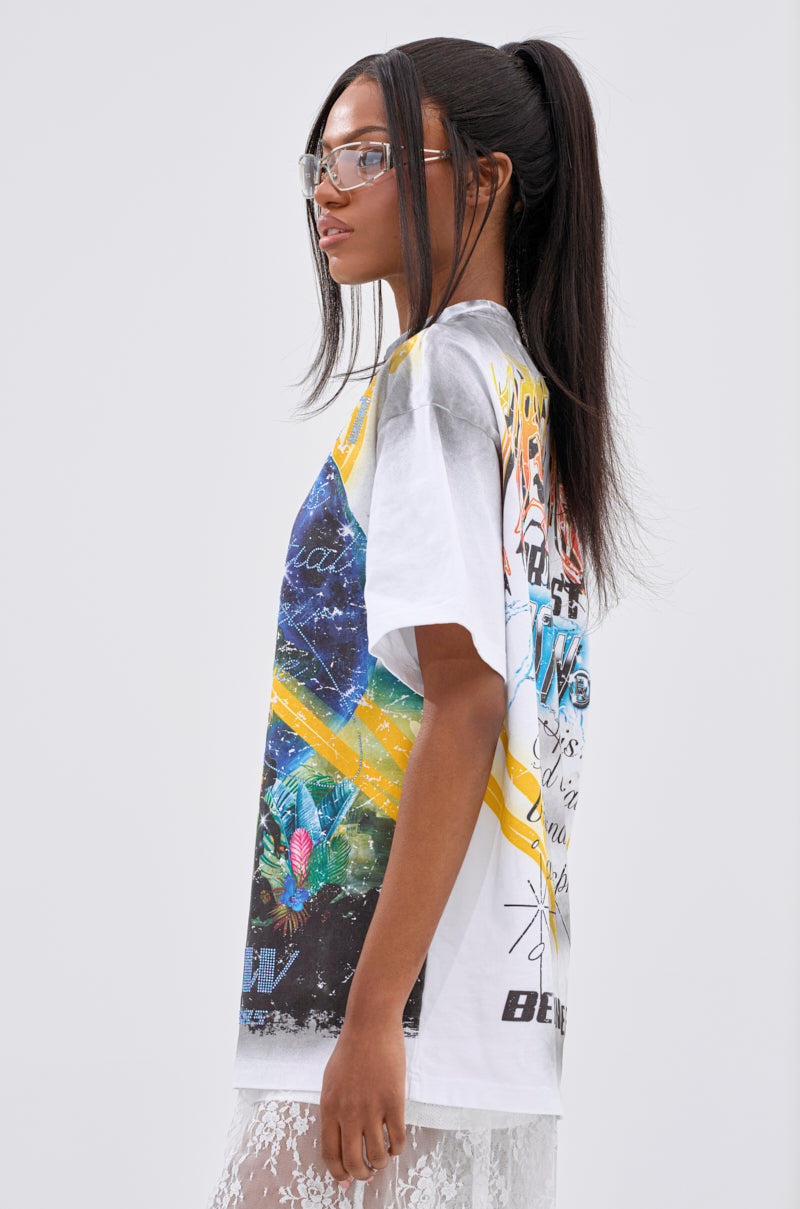 A woman with long, straight hair in a high ponytail wears clear glasses, the NEW WORLD OVERSIZED GRAPHIC TEE featuring a planetary motif, and a white lace skirt. She stands sideways against a plain light background, looking forward.