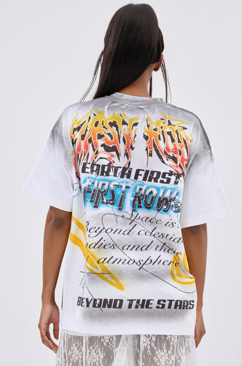 A person with long hair faces away, wearing the NEW WORLD OVERSIZED GRAPHIC TEE with colorful text, yellow accents, a planetary motif, and bold cursive streetwear style featuring "FIRST ROW" and "BEYOND THE STARS.