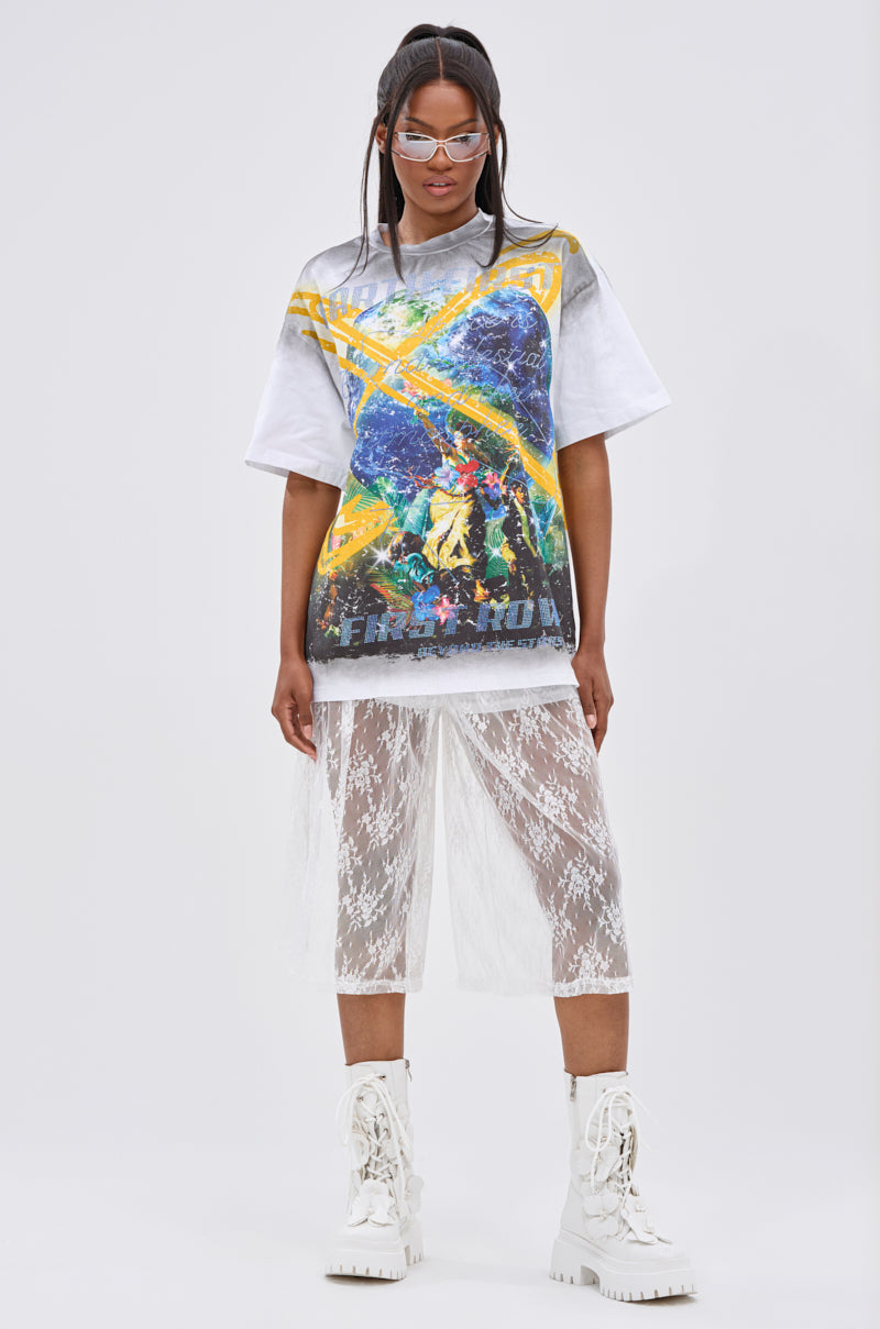 A woman faces forward wearing clear glasses, the NEW WORLD OVERSIZED GRAPHIC TEE with a planetary design, a white lace skirt over white shorts, and white lace-up boots against a plain background.